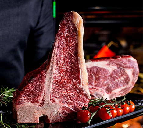 Pièce de bœuf d'exception à l'os (type T-bone) présentée avec des tomates cerises et du romarin frais dans notre boucherie à Bordeaux.