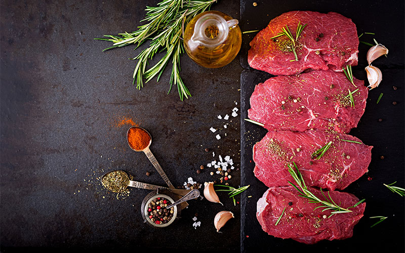 Assortiment de steaks de bœuf premium assaisonnés aux herbes, poivre et ail, prêts pour la grillade à la Boucherie Nador.